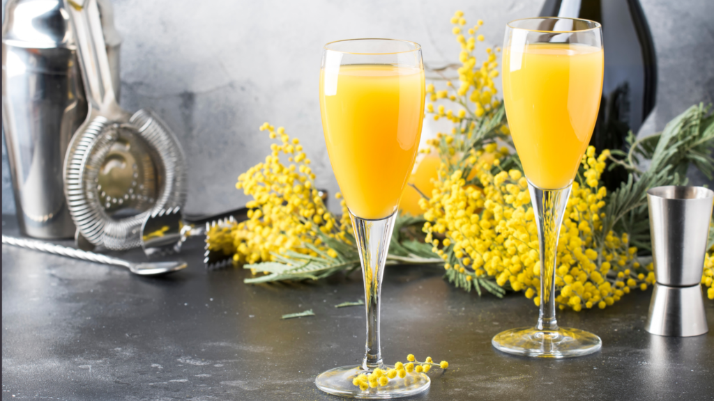 Two glasses of mimosas in front of cocktail equipment on a table